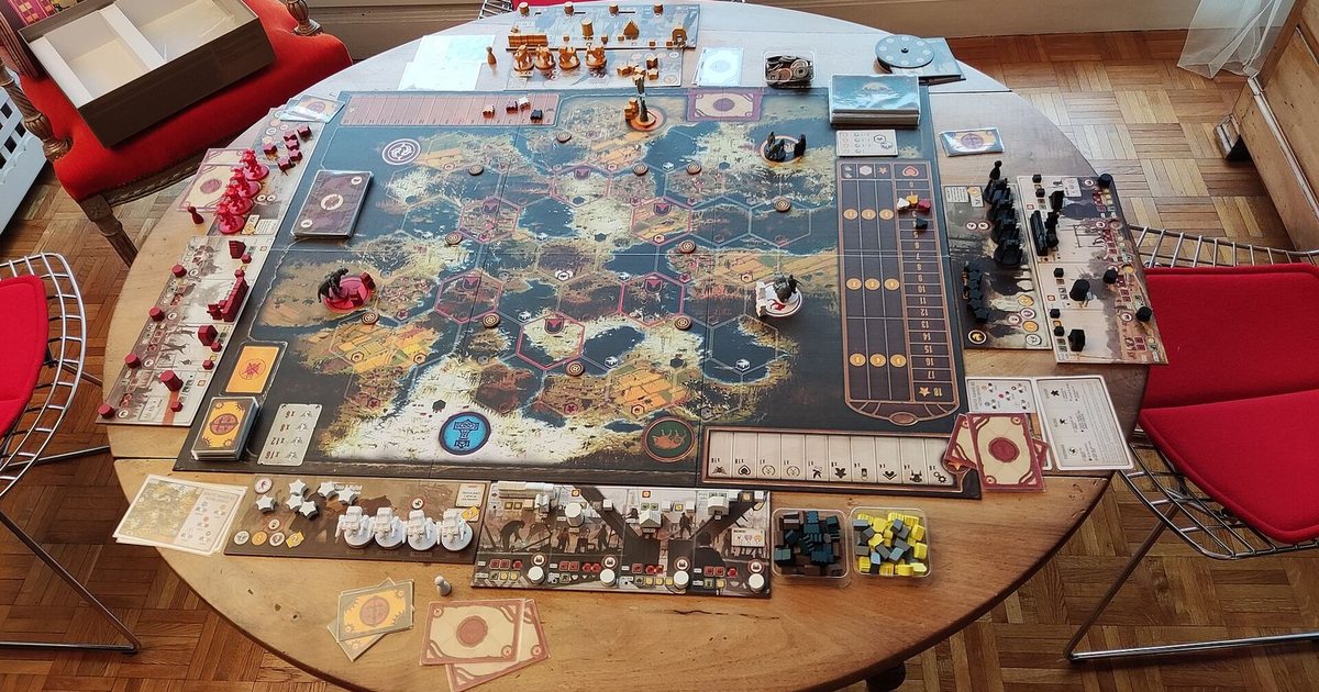 A game of Scythe set up on a round wooden table, red chairs around it