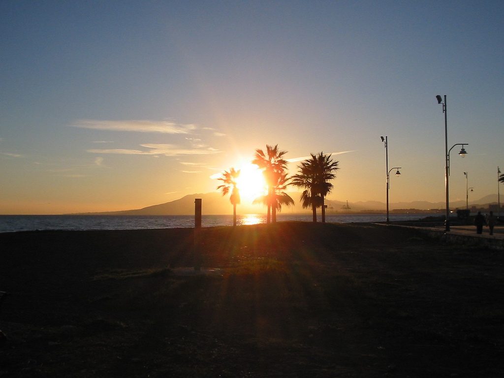 Palm trees in silhouette on the beach at El Palo, Málaga, the sun setting behind the hills